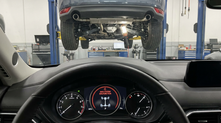 Modern Mazda dashboard with a warning light illuminated and the front axle system highlighted in a professional automotive repair setting.